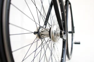 A close-up of a high-quality bicycle wheel with a sleek carbon fiber rim, silver hub, and black spokes, mounted on a clean white background with soft natural lighting, emphasizing texture and precision engineering