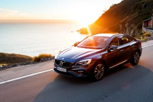 A modern, high-quality car parked on a scenic coastal road at sunset, with soft golden light reflecting off its polished surface, surrounded by gentle hills and a calm ocean in the background, emphasizing elegance, reliability, and premium automotive choice