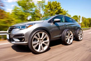 A set of modern, fuel-efficient car wheels with aerodynamic design, mounted on a compact sedan driving on a sunny highway, surrounded by green trees and clear sky, symbolizing cost savings through reduced fuel consumption