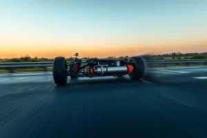 A modern car driving smoothly on a wet highway at dusk, with visible suspension components absorbing road imperfections, motion blur on wheels to convey stability, soft reflections on the asphalt, and a clear view of the vehicle's chassis and tires maintaining firm contact with the road — emphasizing enhanced handling and shock absorption