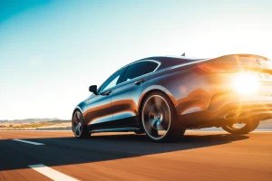 A set of high-quality car wheels with sleek, modern design, mounted on a luxury sedan driving smoothly on a sunlit highway at golden hour, conveying comfort and confidence through motion blur and soft reflections on the rims, with a clear blue sky and gentle landscape in the background