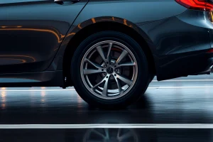 A set of high-performance car wheels with sleek metallic rims and deep tread tires, mounted on a luxury sedan driving smoothly on a wet asphalt road at dusk, reflecting city lights, conveying confidence and control in motion, shallow depth of field, realistic lighting, no text or symbols