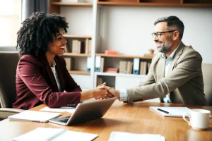 A warm, professional office scene showing a consultant sitting across from a diverse client at a wooden desk, exchanging a handshake with a smile, soft natural light from a window, books and a laptop visible in the background, subtle details like a coffee cup and notepad, conveying personalized attention and trust