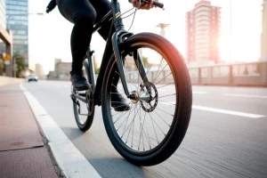 A modern urban cyclist riding a sleek city bicycle with a well-designed wheel in focus, showing smooth spokes, a durable rim, and a high-quality tire suitable for pavement, set against a clean city street with subtle background elements like bike lanes, distant buildings, and soft daylight; the wheel is the central subject, slightly blurred background to emphasize depth and detail