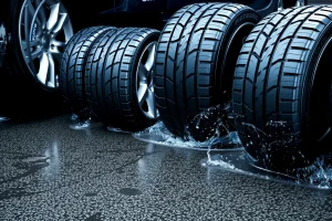 A set of high-performance car tires with deep tread patterns and aggressive sidewall design, mounted on alloy wheels, positioned on a wet asphalt road with visible water spray and tire marks, emphasizing superior traction and grip, realistic lighting with reflections on the wet surface, no text or logos