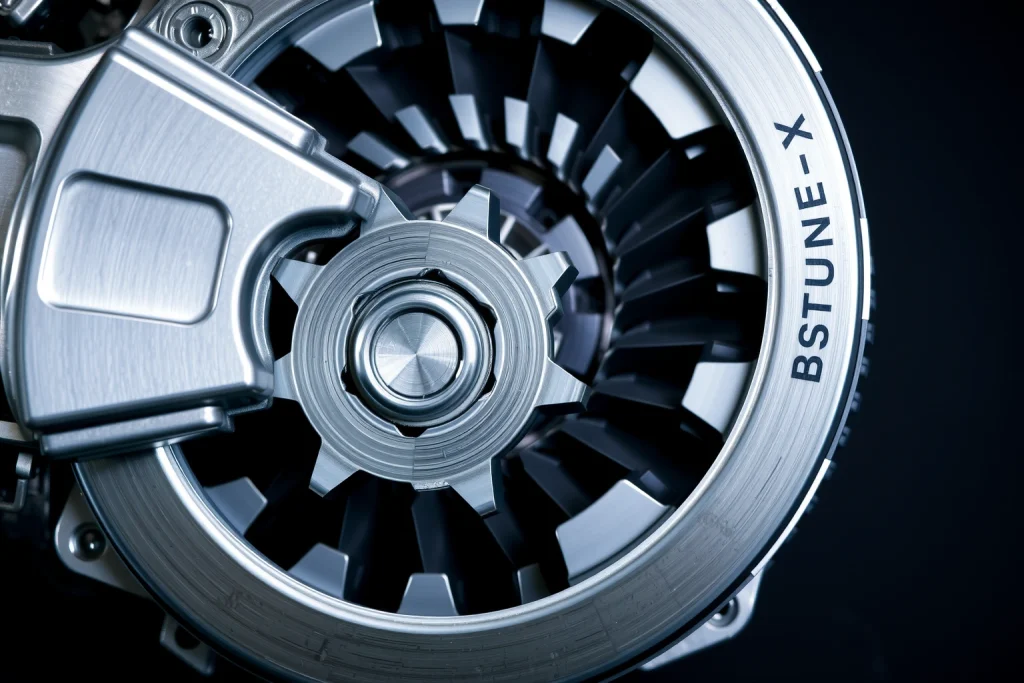 A close-up of a precise mechanical clutch mechanism from the Koleso-Bestune brand, showing interlocking metal gears and friction plates with high detail, clean industrial lighting, metallic surfaces reflecting subtle highlights, isolated on a dark gray background, emphasizing engineering precision and reliability