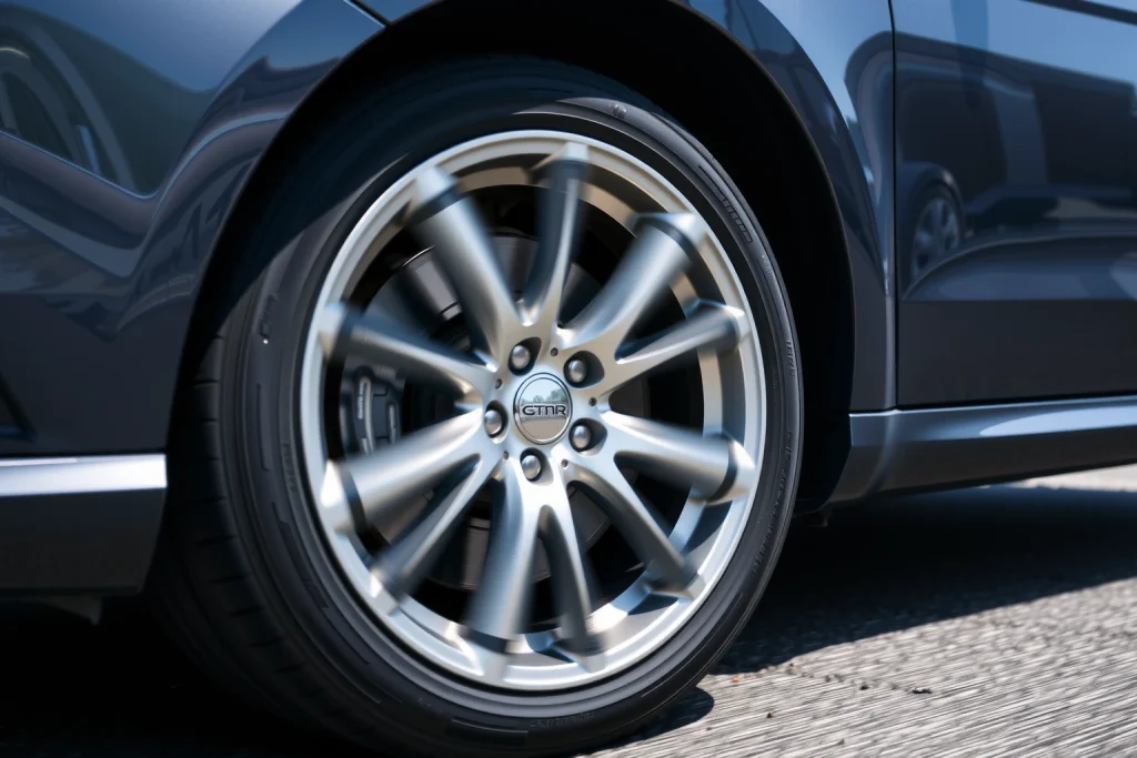 A close-up of a modern car with lightweight alloy wheels, showing the wheels in detail with a sleek metallic finish, set on a clean urban road under bright daylight, emphasizing the reduced weight and aerodynamic design of the wheels, with subtle motion blur to suggest performance, no text or labels visible